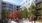 a couple people sitting on a bench in front of a building with trees throughout a courtyard